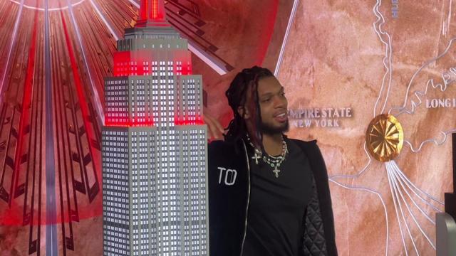 Damar Hamlin stands next to a model of the Empire State Building lit in red. 