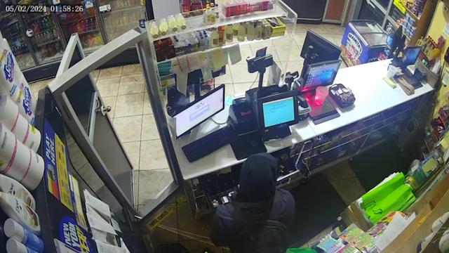 Surveillance footage from inside a bodega shows a hooded individual behind an open cash register. 