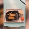 A photo of a school lunch on a tray consisting of five mozzarella sticks, an orange and a container of an unknown food. 