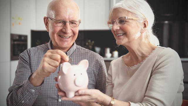 Senior couple puts the coin into the piggybank 