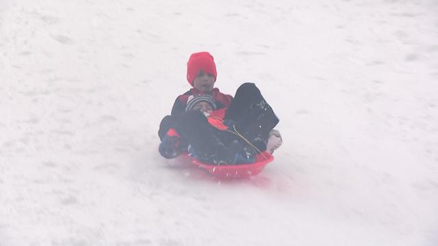 Two children ride a red plastic sled down a snowy hill. 