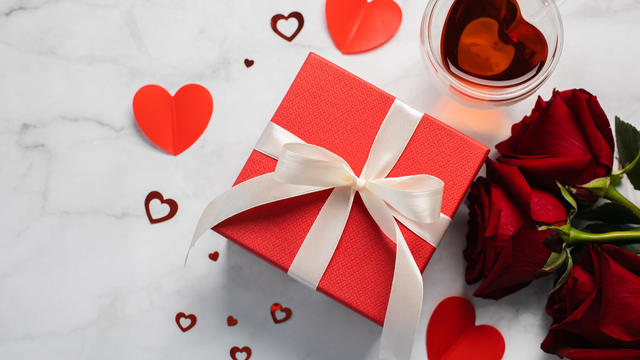 Valentine's Day background. Gift box, red roses, hot tea in cup and aper hearts on background. Flat lay, directly above, copy space. 