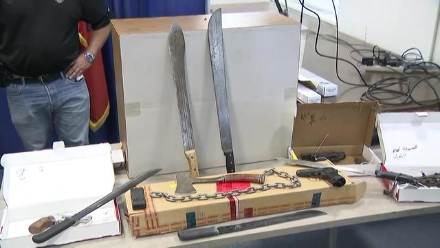 Machetes, chains, an axe and other weapons on display on a table. 