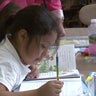 A New York City elementary school student writes in a notebook in a classroom. 