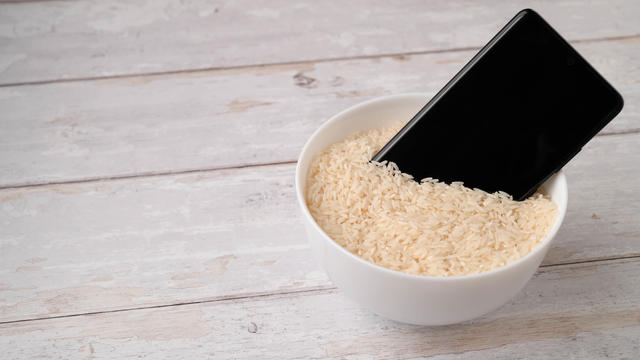 A mobile phone placed to dry in a bowl full of rice after the phone fell into water. Light wooden table background. 