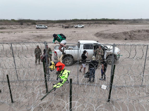 An aerial view shows a group of migrants climbing up wire fences in Eagle Pass, Texas, on Feb. 28, 2024.