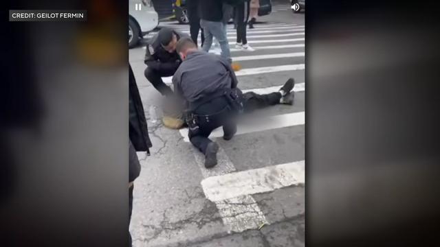 Two NYPD officers crouch over a teenager laying in a New York City crosswalk. 