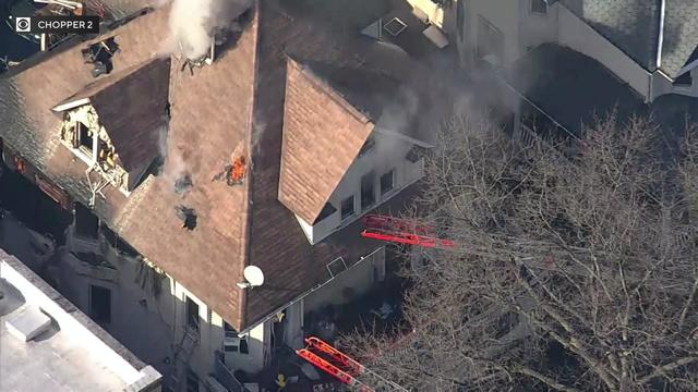 An aerial view of a home in the Bronx. Flame and smokes can be seen through multiple holes in the roof. 