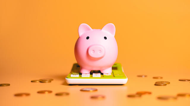 A piggy bank over a green calculator with scattered coins isolated on orange background in studio photography. Concepts of saving money, finance and investments. 