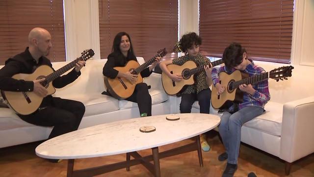 Jason, Elysa, Joseph and Noah Hochman sit on a couch, each playing an acoustic guitar. 