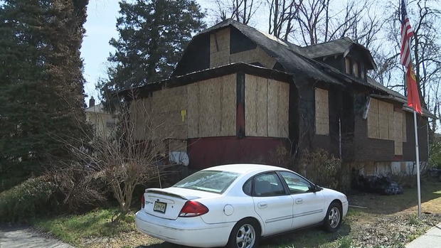 A home is boarded up after a fire; a car sits out front. 