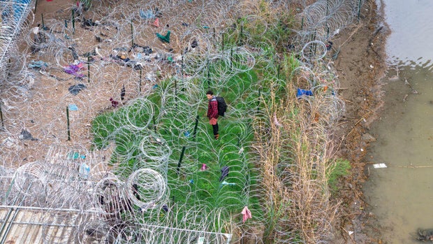 In an aerial view, an immigrant faces coils of razor wire after crossing the Rio Grande from Mexico on March 17, 2024 in Eagle Pass, Texas.