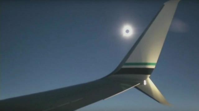 A total solar eclipse is visible over the wing of a plane in flight. 