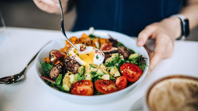 Close up shot of a woman eating a dish of fresh beef cobb salad with a soft boiled egg and coffee at a cafe table. Enjoying her healthy and nutritious lunch. Maintaining a healthy and well-balanced diet. The concept of healthy eating lifestyle 