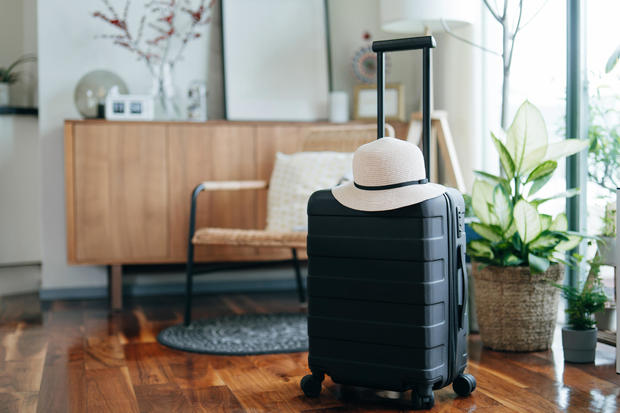 Still life of a black suitcase with a straw hat in the living room of an apartment. Travel and vacation concept 