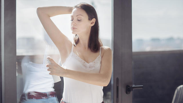 Adult woman using deodorant in new modern living room 