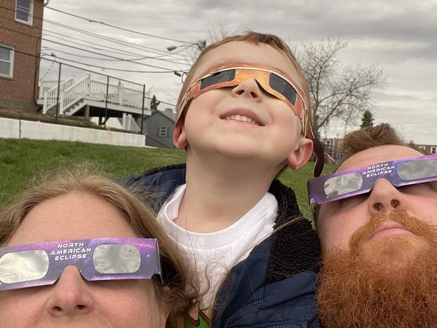 Three people look up at the sky through eclipse glasses 