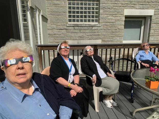 Four women watch the eclipse on a deck 