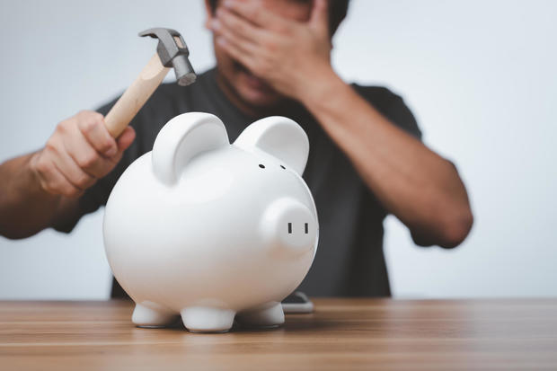 Male hand with hammer about to smash piggy bank to get at savings. 