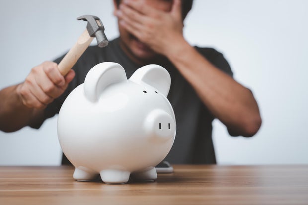 Male hand with hammer about to smash piggy bank to get at savings.
