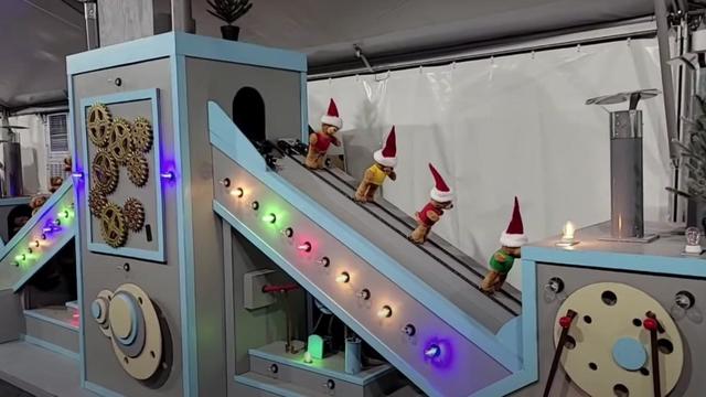 A holiday light display shows teddy bears with Santa hats on a conveyer belt. 