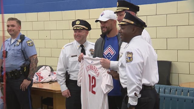 Kyle Schwarber holds his jersey while posting for a photo with three Philadelphia police officers. 