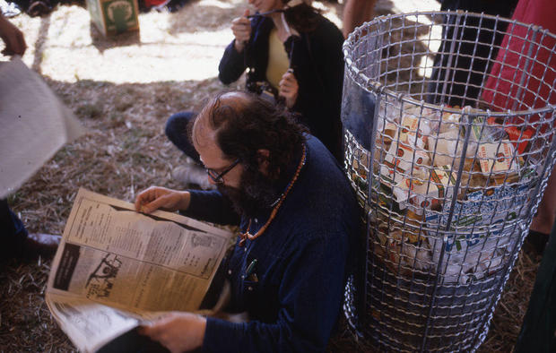 View of American Beat poet Allen Ginsberg (1927-1997) as he sits on the ground and reads a newspaper during the first Earth Day celebration in Philadelphia on April 22, 1970. He leans against a wire waste basket. 