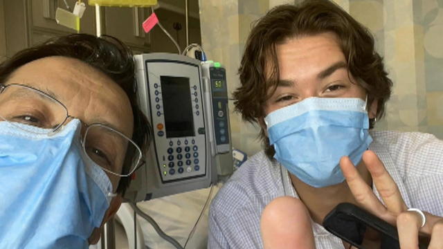 Two people wearing masks take a selfie in a hospital room 