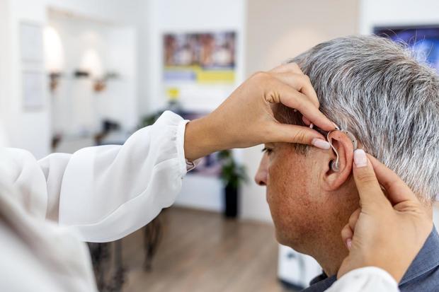 Female doctor fitting a mature male patient with a hearing aid 