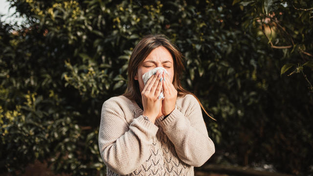 young woman suffering spring allergy and blowing nose with a tissue in nature 