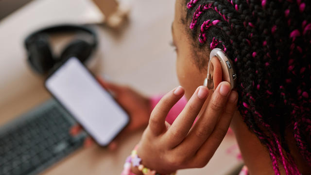 Close up of black teenage girl wearing hearing aid on ear 