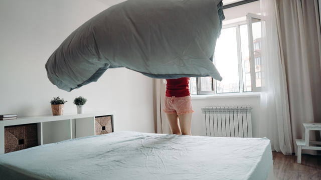 A woman makes her bed, the sheet billowing in the air above the mattress. Household chores, housewife or housekeeper cleaning the apartment 
