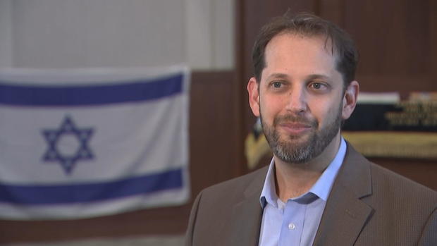 Rabbi Micah Peltz during an interview with CBS News Philadelphia; an Israeli flag hangs in the background 