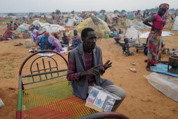 Adam Hassan, who has an album with pictures of his son and father, who he said were killed by the RSF and Arab militias in the West Darfur town of Murnei in June, sits outside his makeshift shelter in Adre 