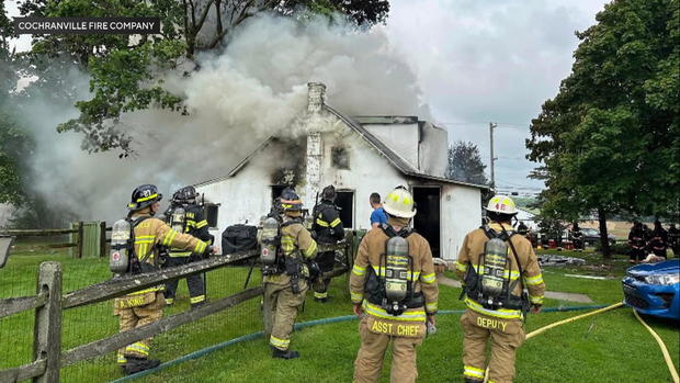 Firefighters stand near a house on fire 