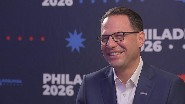 Gov. Josh Shapiro smiles during an interview in front of a sign that says Philadelphia 2026 
