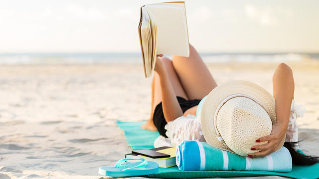 Woman lies on the beach reading a book 