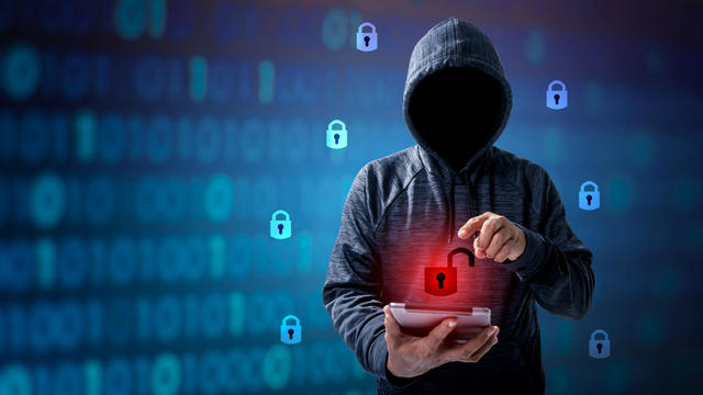 Hacker in hoodie dark theme Hacker in a blue hoody standing in front of a coding background with binary streams and information security terms cybersecurity concept 