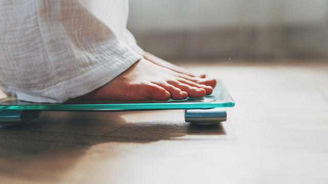 Female feet standing on electronic scales for weight control on wooden background. The concept of slimming and weight loss 