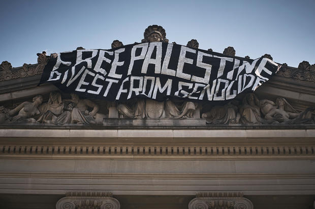 A pro-Palestinian demonstrator, upper left, hangs a flag on top of the Brooklyn Museum during a protest demanding a permanent cease-fire in Gaza, Friday, May 31, 2024, in New York. 
