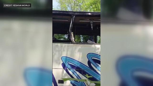 A photo of a tour bus with passenger side windows smashed and other damage. 
