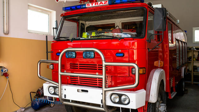 The front of the truck of an old Polish fire truck with visible blue light signals, water cannon and the Polish word "STRAZ". 