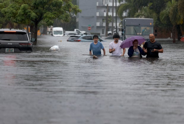 People walk through a flooded street as they evacuate on June 12, 2024, in Hollywood, Florida.