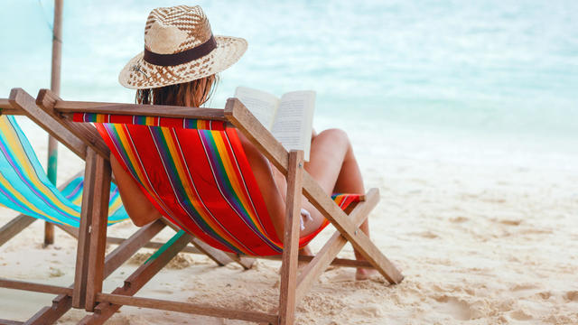 View from behind of a woman reading while sitting on beach 