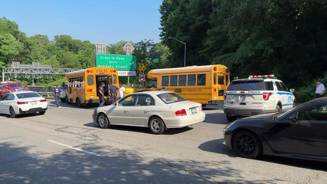 Two small school buses sit on the side of a road near an NYPD vehicle. 