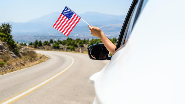 Woman holding USA flag from the open car window driving along the serpentine road in the mountains. Concept 