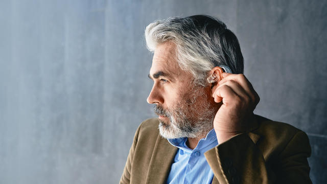Grey-haired mature man with hearing impairment using hearing aid. Hearing solutions for deafness people 