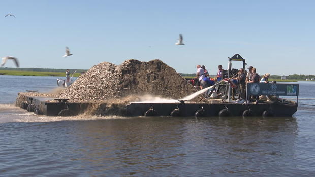 Workers spray oyster shells off of a boat and into the Mullica River 