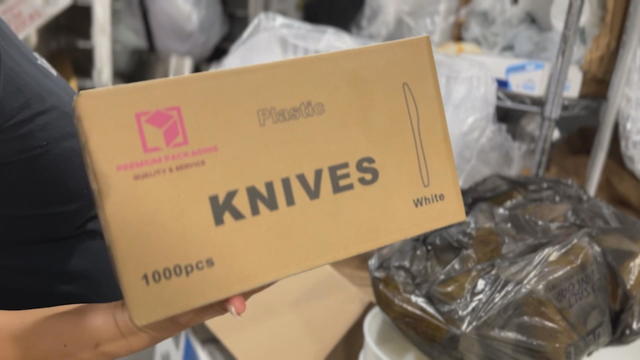 A worker at KOP Pizza holds a cardboard box of plastic knives 