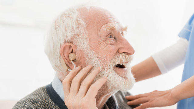 Profile of happy and cheerful man with hearing aid in ear, looking away 